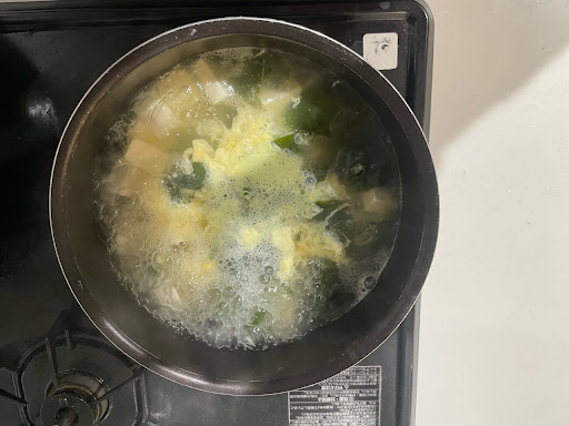 煮立ったスープに豆腐を入れ、卵を回しいれた写真。