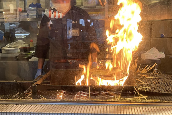 店先でカツオの藁焼きの風景が見られる。大きな炎があがっている。